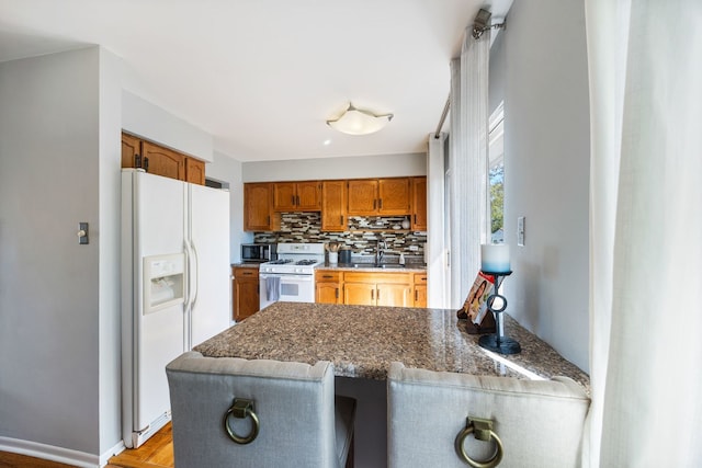 kitchen with sink, backsplash, kitchen peninsula, dark stone countertops, and white appliances