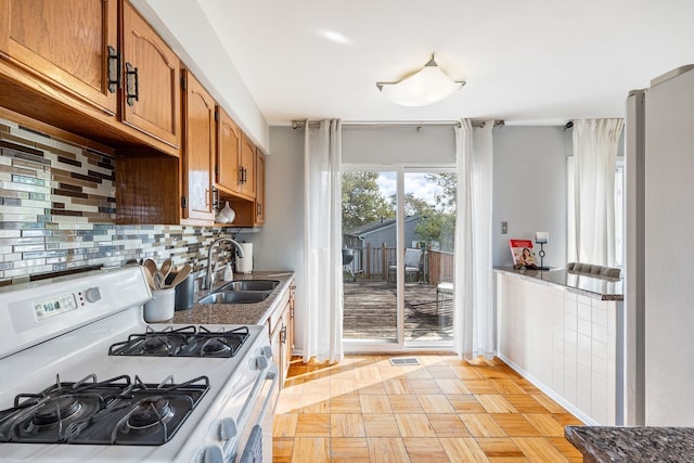 kitchen featuring backsplash, white range with gas cooktop, sink, and light parquet floors