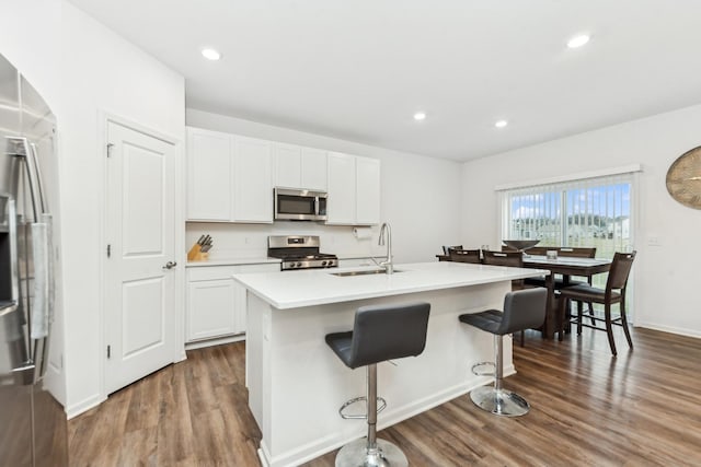 kitchen featuring stainless steel appliances, a kitchen island with sink, sink, dark hardwood / wood-style floors, and white cabinetry