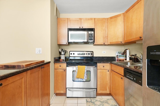 kitchen with dark stone countertops, sink, light tile patterned flooring, and appliances with stainless steel finishes