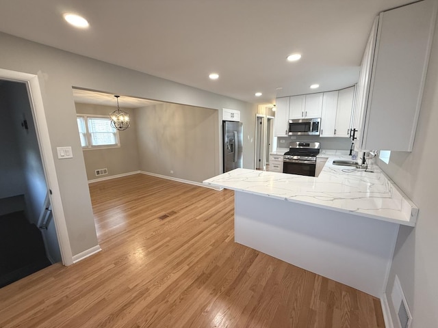 kitchen featuring white cabinets, light hardwood / wood-style flooring, appliances with stainless steel finishes, kitchen peninsula, and a chandelier