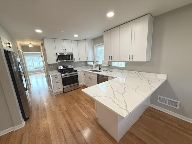 kitchen with white cabinets, light stone countertops, kitchen peninsula, and stainless steel appliances