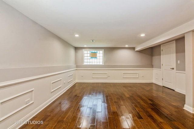 empty room featuring recessed lighting, wainscoting, a decorative wall, and dark wood-style flooring