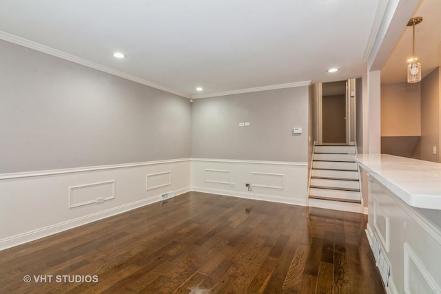 empty room featuring dark wood-style floors, recessed lighting, wainscoting, crown molding, and stairs