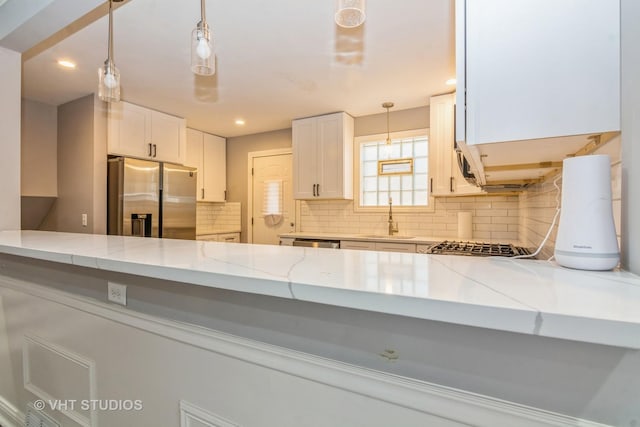 kitchen with tasteful backsplash, decorative light fixtures, light stone counters, stainless steel appliances, and a sink