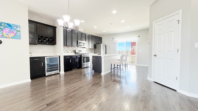 kitchen featuring a center island with sink, hanging light fixtures, appliances with stainless steel finishes, tasteful backsplash, and beverage cooler