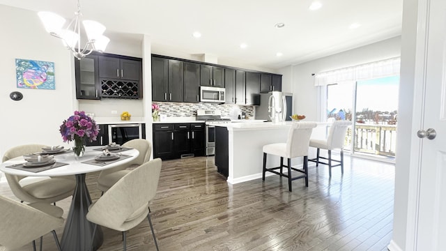 kitchen with pendant lighting, backsplash, hardwood / wood-style flooring, an island with sink, and stainless steel appliances