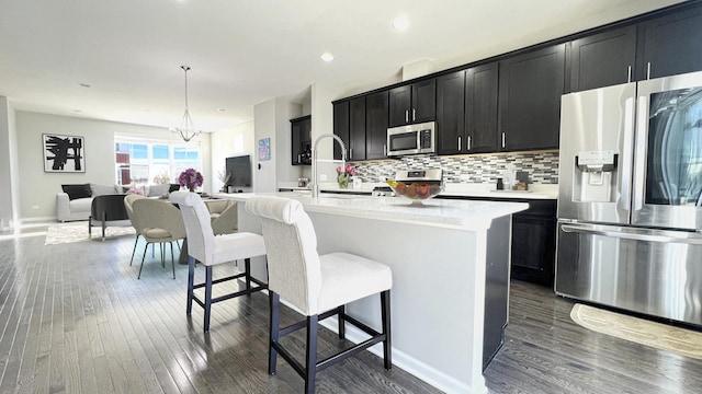 kitchen with a breakfast bar, a kitchen island with sink, hanging light fixtures, and stainless steel appliances