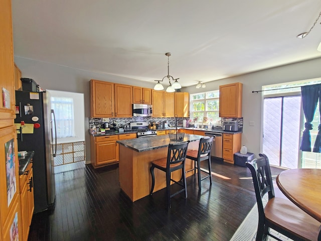 kitchen featuring hanging light fixtures, a kitchen breakfast bar, dark hardwood / wood-style floors, a kitchen island, and appliances with stainless steel finishes