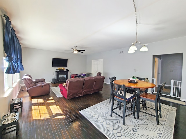 dining space with ceiling fan with notable chandelier and dark wood-type flooring