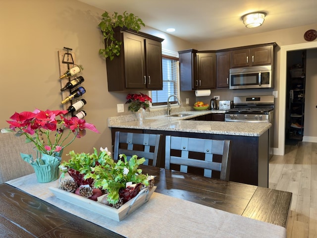 kitchen with sink, light hardwood / wood-style flooring, dark brown cabinets, kitchen peninsula, and stainless steel appliances