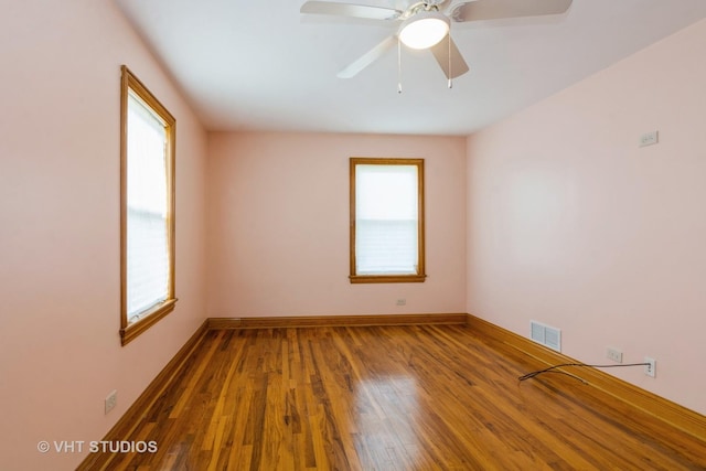 spare room with ceiling fan, visible vents, baseboards, and wood finished floors