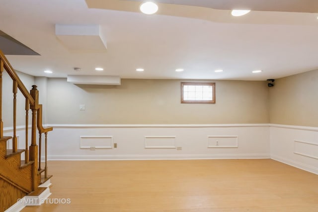 below grade area with a wainscoted wall, stairway, recessed lighting, and light wood-type flooring