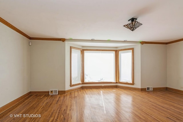 spare room with wood finished floors, visible vents, and ornamental molding