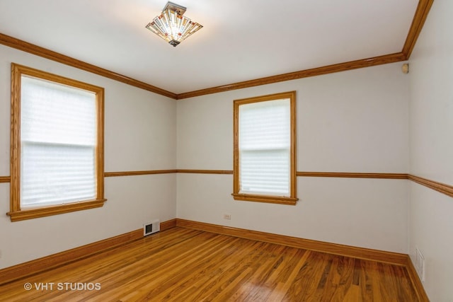 unfurnished room featuring visible vents, ornamental molding, baseboards, and wood finished floors