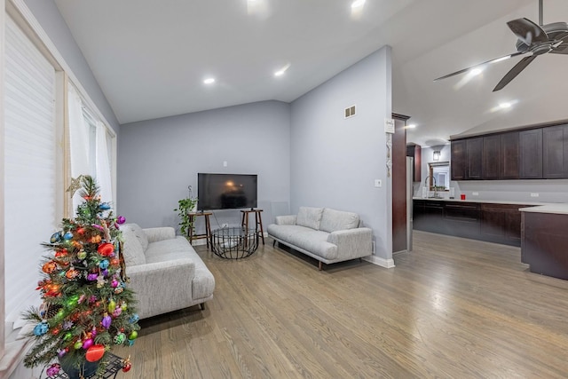 living room with ceiling fan, light wood-type flooring, sink, and vaulted ceiling