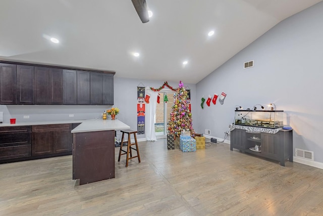 kitchen with a kitchen bar, light wood-type flooring, dark brown cabinets, vaulted ceiling, and a center island