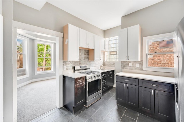 kitchen featuring gas range, sink, dark colored carpet, tasteful backsplash, and white cabinets