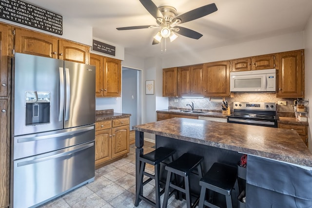 kitchen with backsplash, sink, a breakfast bar area, ceiling fan, and stainless steel appliances