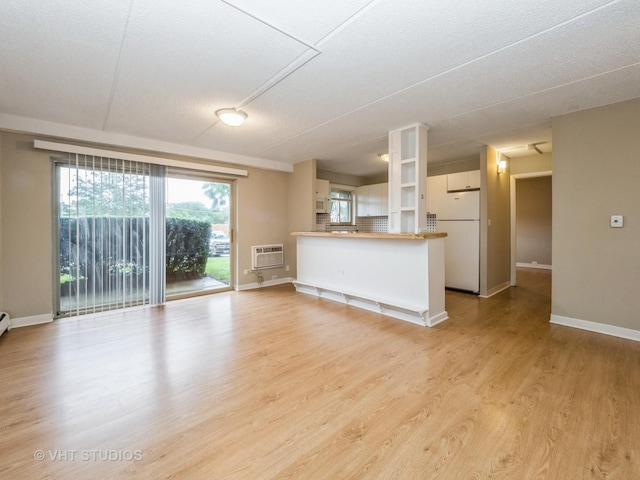 unfurnished living room with a wall mounted air conditioner and light hardwood / wood-style floors