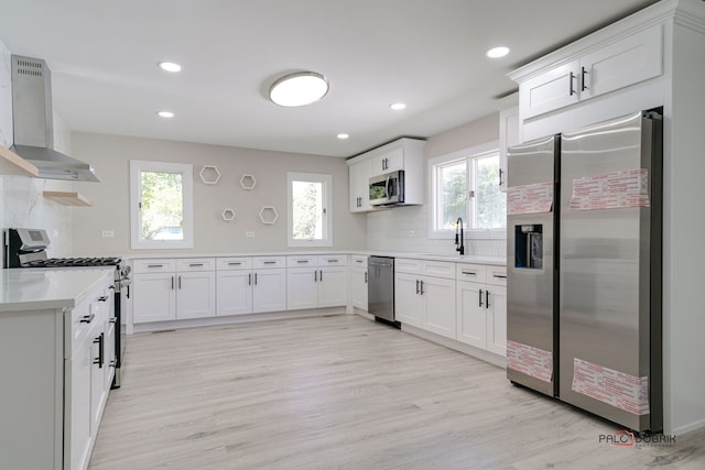 kitchen with wall chimney range hood, decorative backsplash, appliances with stainless steel finishes, plenty of natural light, and white cabinetry