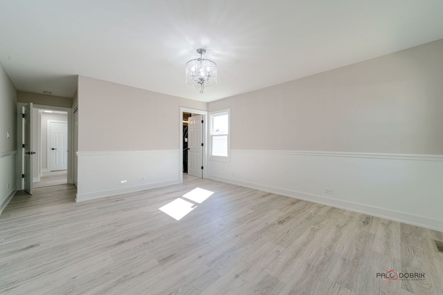 spare room with light wood-type flooring and a notable chandelier