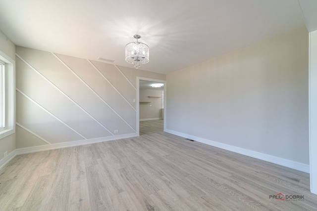 unfurnished room featuring light wood-type flooring and a notable chandelier