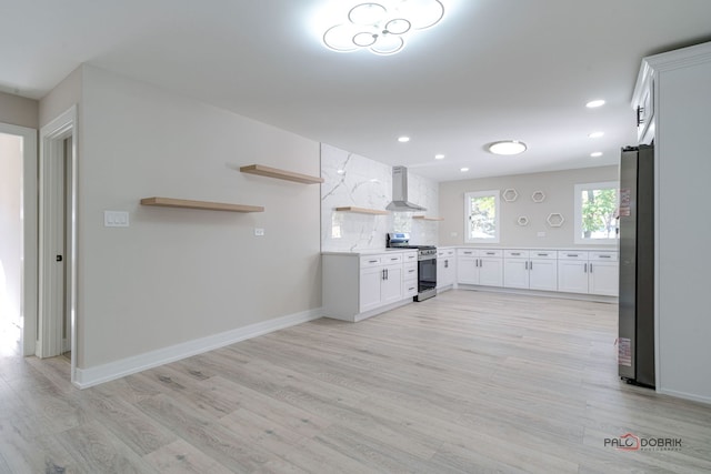 kitchen featuring white cabinets, wall chimney range hood, decorative backsplash, light wood-type flooring, and appliances with stainless steel finishes