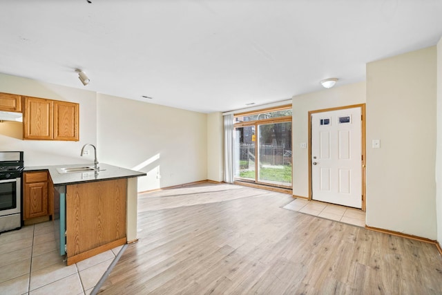 kitchen with kitchen peninsula, sink, stainless steel range oven, and light wood-type flooring