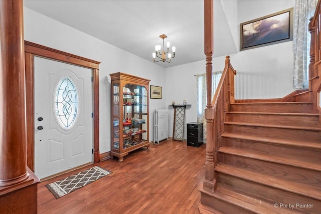 entrance foyer featuring hardwood / wood-style flooring, radiator heating unit, decorative columns, and a chandelier