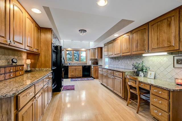 kitchen featuring black appliances, a raised ceiling, light wood-type flooring, light stone countertops, and tasteful backsplash