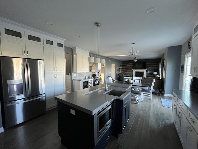 kitchen featuring appliances with stainless steel finishes, a kitchen island with sink, dark wood-type flooring, pendant lighting, and white cabinetry