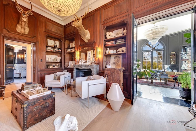 sitting room featuring built in features, a towering ceiling, ornamental molding, light wood-style floors, and a chandelier