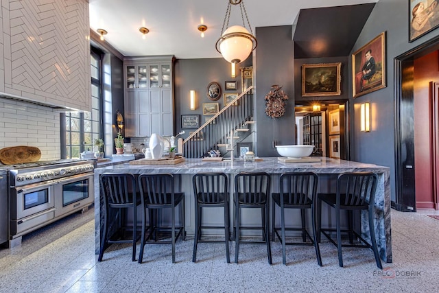 kitchen with light speckled floor, double oven range, decorative backsplash, a kitchen bar, and glass insert cabinets