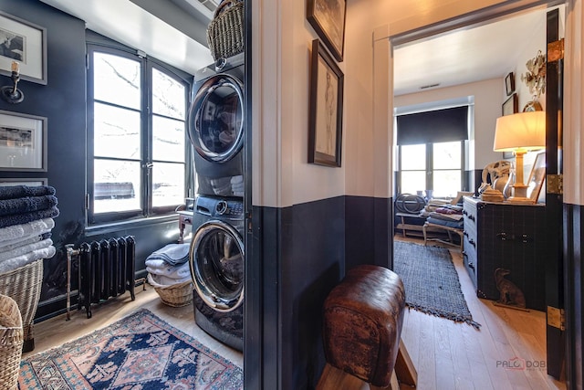 washroom with laundry area, light wood finished floors, radiator heating unit, and stacked washer / drying machine