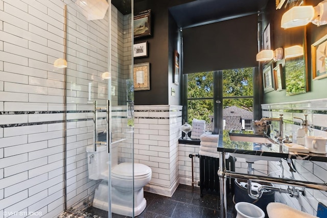 full bath featuring toilet, a wainscoted wall, granite finish floor, tile walls, and a stall shower