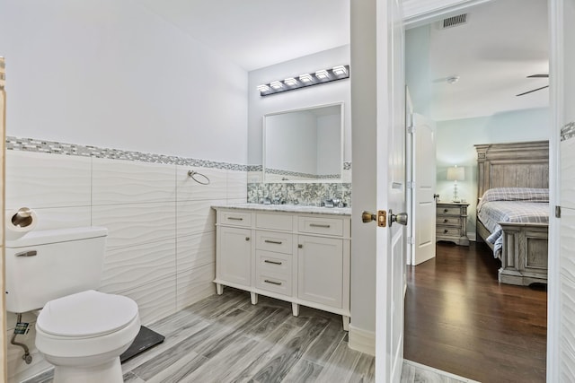 bathroom with vanity, ceiling fan, hardwood / wood-style flooring, tile walls, and toilet