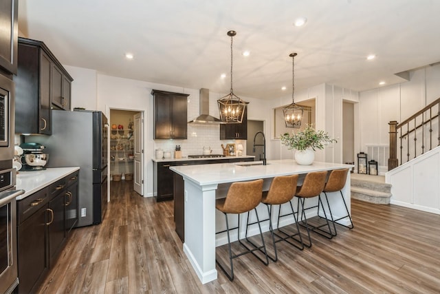 kitchen with a kitchen island with sink, decorative light fixtures, sink, tasteful backsplash, and wall chimney range hood