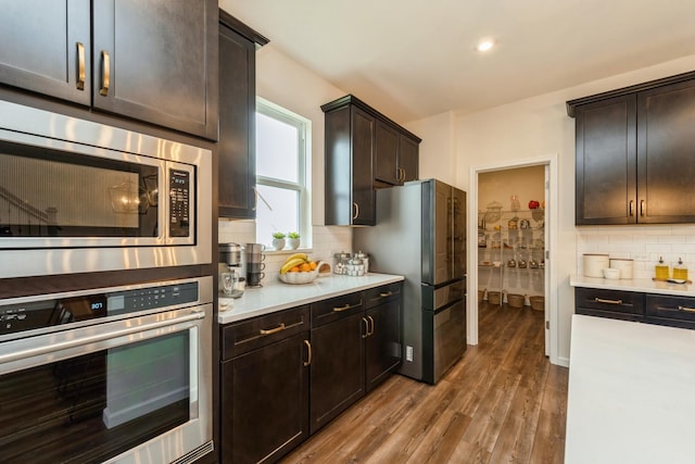 kitchen with appliances with stainless steel finishes, decorative backsplash, dark brown cabinets, and wood-type flooring