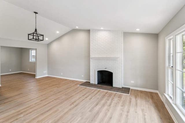 unfurnished living room with a wealth of natural light, a fireplace, lofted ceiling, and light wood-type flooring