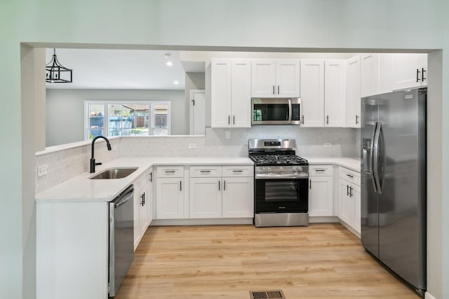 kitchen with backsplash, sink, light hardwood / wood-style flooring, appliances with stainless steel finishes, and white cabinetry