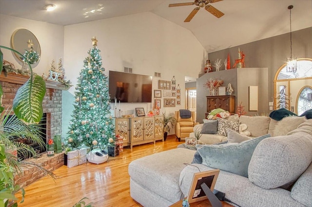 living room with ceiling fan, hardwood / wood-style floors, vaulted ceiling, and a brick fireplace