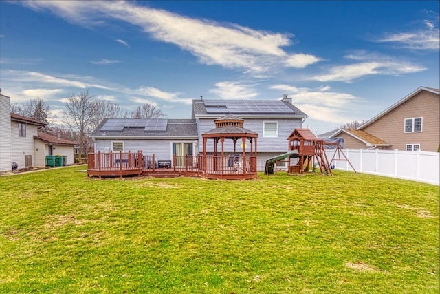 rear view of property with a yard, a gazebo, a playground, solar panels, and a deck