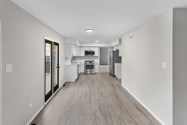 kitchen featuring french doors, light wood-type flooring, stainless steel appliances, sink, and white cabinets