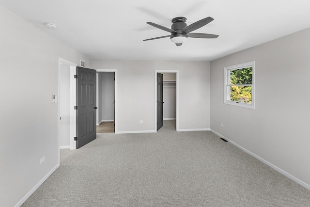 unfurnished bedroom featuring ceiling fan, a walk in closet, light carpet, and a closet