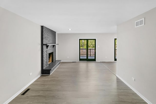 unfurnished living room featuring wood-type flooring and a brick fireplace