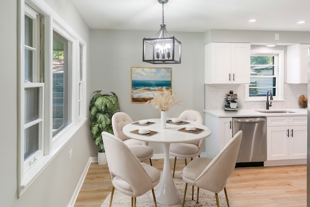 dining space featuring sink, light wood-type flooring, plenty of natural light, and an inviting chandelier