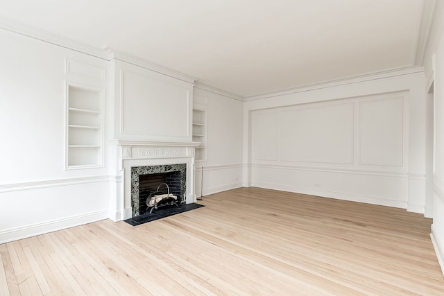 unfurnished living room with built in features, a high end fireplace, light wood-type flooring, and ornamental molding