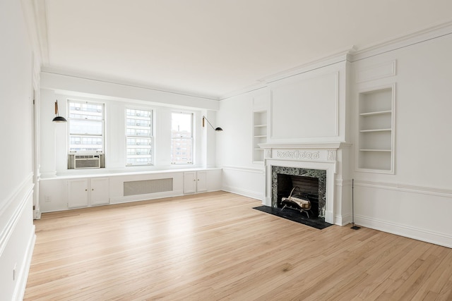 unfurnished living room featuring built in features, crown molding, cooling unit, a fireplace, and light wood-type flooring