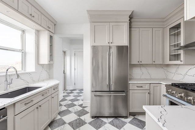 kitchen with sink, wall chimney range hood, premium appliances, light stone counters, and decorative backsplash